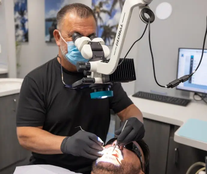 A focused male clinician wearing a face mask and using a high-powered dental operating microscope